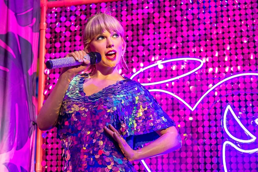 Taylor Swift smiling with a hand on her hip while performing in London