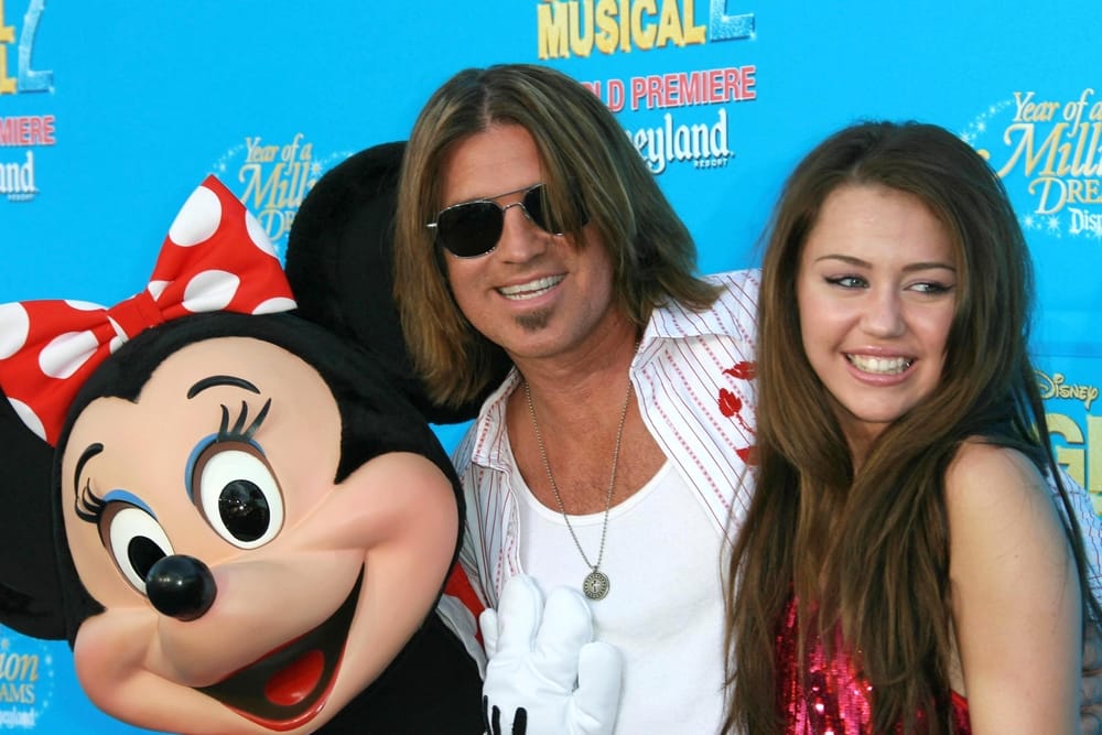 Miley Cyrus smiling next to her dad and Minnie Mouse